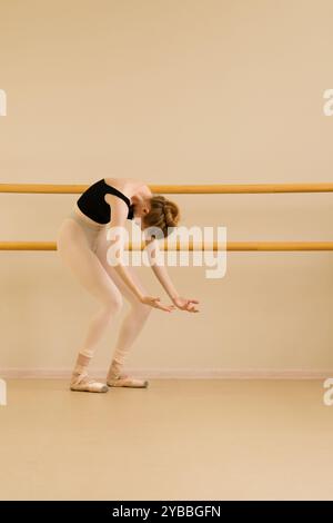 Ballerina di balletto che si piega in avanti alla sbarra, estendendo le braccia in un arco grazioso. Foto Stock