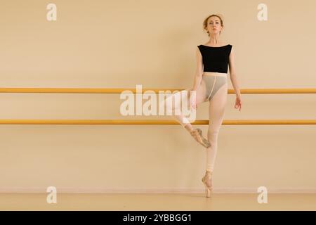 Ballerina di balletto in una posa concentrata alla sbarra, alzando con grazia una gamba. Foto Stock