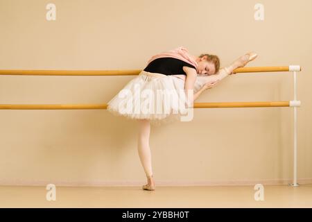 Una ballerina si allunga con la gamba sulla sbarra, appoggiando con grazia il suo corpo in una posizione calma e concentrata. Foto Stock