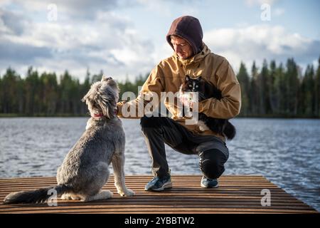 Uomo con cane e gatto seduto su un molo di legno Foto Stock