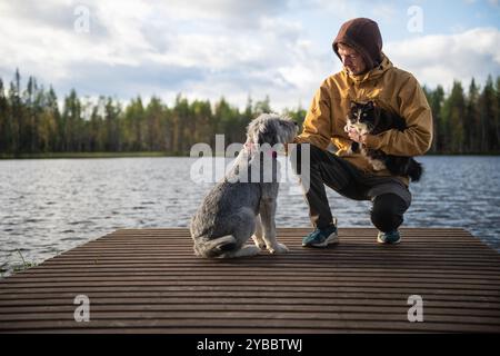 Uomo con cane e gatto seduto su un molo di legno Foto Stock