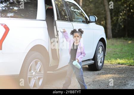 Ragazza eccitata in giacca lavanda che apre la porta dell'auto, che tiene l'acqua Foto Stock