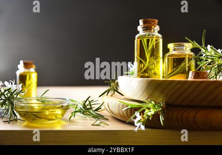 Olio essenziale di rosmarino in bottiglie di vetro con ramoscelli freschi su un tavolo di legno. Vista frontale. Foto Stock