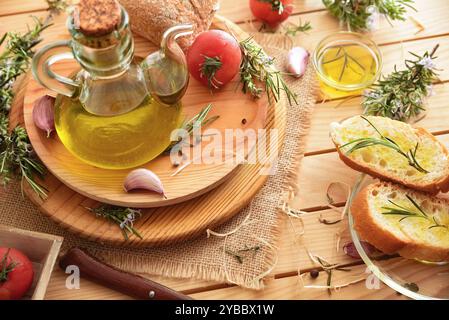 Bottiglia e recipiente con olio essenziale di rosmarino su banco di legno con cibo e rametti di rosmarino in natura. Vista rialzata. Foto Stock