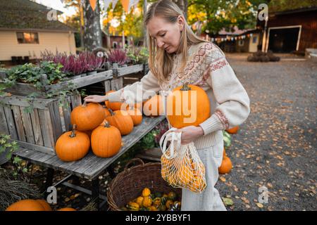 Donna che tiene in mano una zucca grande e zucche decorative in una borsa in rete Foto Stock
