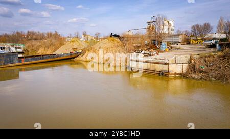 Molo, molo di cemento sulla costa del fiume con rifiuti accumulati di vecchia grande nave, chiatta, nave smantellata a pezzi, tagliare il metallo arrugginito per scarpa, utilizzando l'aria condizionata Foto Stock