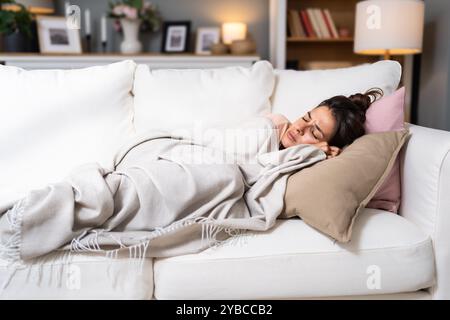 Donna che dorme sul divano a casa riposando avvolgendo in plaid sentendo i sintomi cattivi. Ragazza che soffre di influenza stagionale o raffreddore. Sentiti malsano con influenz Foto Stock