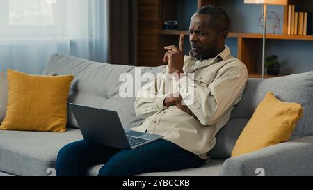 Premuroso uomo d'affari afro-americano, freelance che lavora su un computer portatile a casa, pensa a risolvere i problemi aziendali seriamente pensive Foto Stock