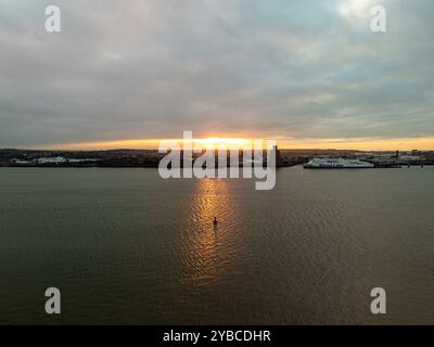 Tramonto arancione che illumina il fiume mersey a liverpool con un traghetto attraccato al molo e lo skyline della città sullo sfondo Foto Stock