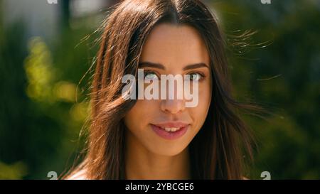 Primo piano sorridente felice attraente donna ispanica che guarda lo stand della macchina fotografica nel parco cittadino in strada, estate, giorno di sole, bella e sicura araba Foto Stock