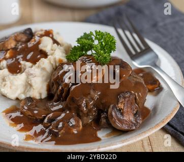 Bistecca di Salisbury con sugo di funghi guarnita con prezzemolo e purè di patate su un piatto bianco Foto Stock