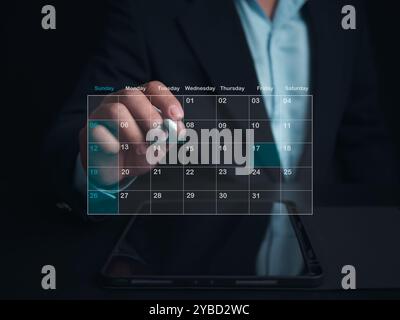 Uomo d'affari che segna le date sul calendario virtuale con un tablet, gestisce il suo programma aziendale, imposta promemoria per appuntamenti importanti, coll creativo Foto Stock