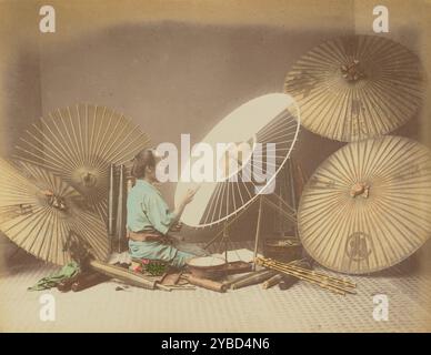 Creatore di ombrelli, anni '1870-'1890 Un creatore di ombrelli si siede su uno sgabello basso, applicando della carta alle costole di un ombrello. Altri ombrelli in varie fasi di assemblaggio sono intorno a lui. Foto Stock