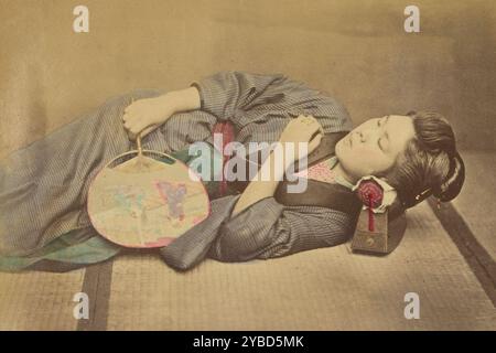 Donna giapponese addormentata che tiene in mano un fan, 1868-1880. Ritratto di una donna sdraiata con gli occhi chiusi. Un takamakura, o poggiatesta, sostiene la testa e tiene un fan in una mano e l'altra sul petto. Foto Stock