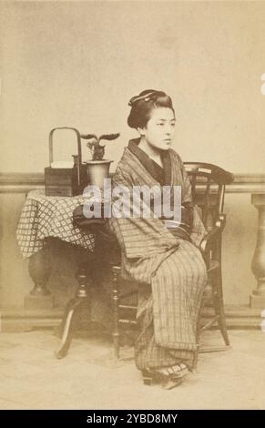 Donna seduta a tavola, circa 1868. Una donna siede su una sedia, sul tavolo accanto a lei c'è un cestino di legno e un albero bonsai. Foto Stock