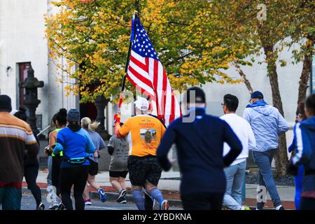 Babylon, New York, USA - 22 ottobre 2024: Vista posteriore di un corridore che porta una bandiera americana mentre corre in una maratona che rappresenta un eroe caduto. Foto Stock