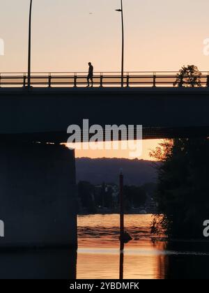 Una figura solitaria cammina attraverso il ponte di Pont Clemenceau durante il tramonto sulla tranquilla Senna a Vernon, Normandia, Francia Foto Stock