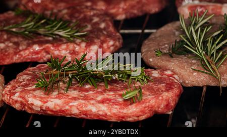 Succulent beef burgers seasoned with sprigs of rosemary, cooking on a grill rack, perfect for a delicious homemade meal or barbecue Foto Stock