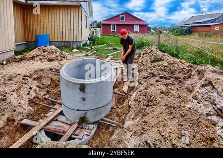Il lavoratore sposta l'anello di cemento pesante utilizzando un piatto a rulli realizzato con tubi in acciaio. Foto Stock