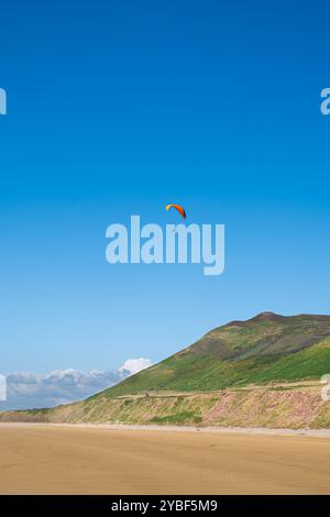 Un parapendio che vola nel cielo blu sopra Rhossili Bay sulla penisola di Gower, Galles del Sud Foto Stock