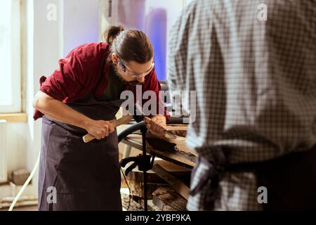 Lavoratore esperto di legno che forma legname grezzo con scalpello e martello in falegnameria, godendo di hobby fai da te. Professionista della lavorazione del legno in studio che forma pezzi di legno con utensili, realizzando sculture in legno Foto Stock