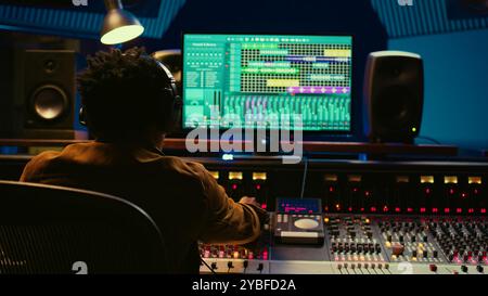 Audio designer che regola l'audio su una scrivania di controllo del mixer, concetto di studio musicale professionale. Il produttore alza il volume e aggiunge effetti su una console di mixaggio, registrando brani dal vivo. Telecamera B.. Foto Stock