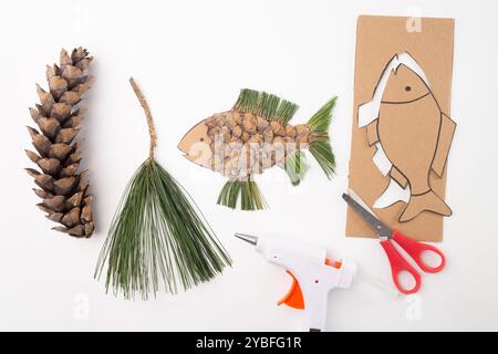 il pesce è realizzato con un pezzo di cartone tagliato a forma di pesce, con piccole scaglie di pino incollate su di esso. Le pinne e la coda sono fatte di ginocchio di pino Foto Stock