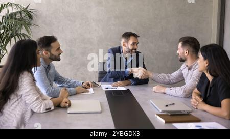 Un CEO soddisfatto e positivo che stringe la mano al dipendente al tavolo Foto Stock