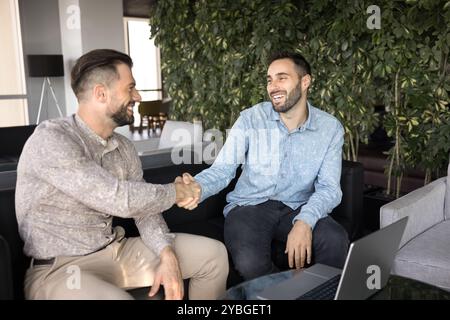 Due allegri imprenditori che stringono la mano durante la riunione in co-working Foto Stock