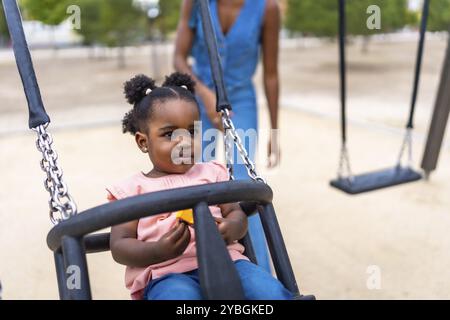 Carina ragazza africana che oscilla nel parco con sua madre Foto Stock