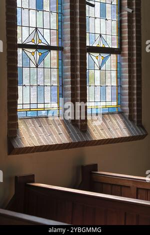 Banchi di legno in una vecchia chiesa olandese con un colorato finestra in vetro colorato Foto Stock