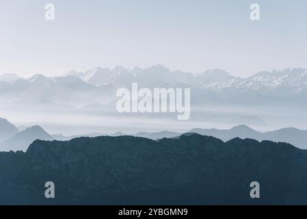 Vista panoramica delle sagome delle montagne nella nebbia mattutina con montagne innevate sullo sfondo. Picos de Europa, Asturie, Spagna, Europa Foto Stock