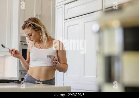 Una bella ragazza bionda si diverte a fare uno spuntino in una cucina bianca a casa Foto Stock