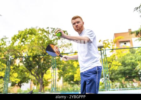 Ritratto con vista dall'angolo basso di un giovane caucasico che gioca a palla in un campo urbano all'aperto Foto Stock