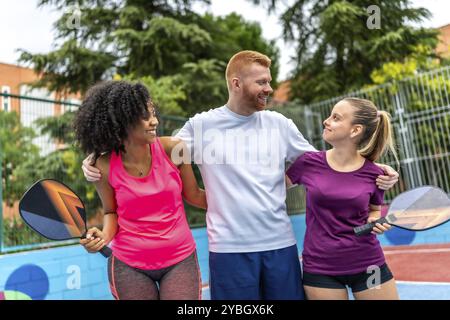 Amici multietnici che abbracciano insieme dopo aver giocato a picnic in un campo all'aperto Foto Stock