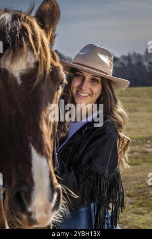 Una bella cowgirl brunetta posa con il suo cavallo prima di un giro in campagna Foto Stock