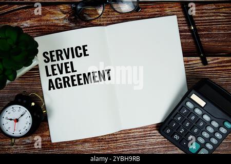 Testo SLA (Service Level Agreement) scritto su carta strappata con calcolo e allarme su sfondo in legno Foto Stock