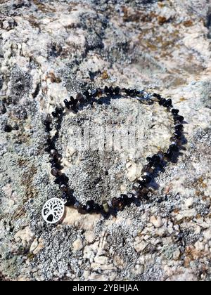 Choker nero in ossidiana con pendente Tree of Life su una superficie di roccia di granito grigio | collana grossa in pietra naturale con il fascino dell'albero della vita Foto Stock