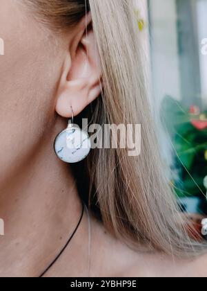 Orecchini rotondi in resina di marmo bianco realizzati a mano con finitura trasparente sui capelli biondi. Collezione di gioielli ispirata alla natura, modello di gioielli, elegante Foto Stock