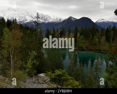 LAC vert, lago alpino circondato da pini, sopra Passy, in alta savoia, e montagne innevate sullo sfondo con clima nuvoloso Foto Stock