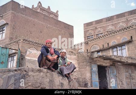 SANAA, YEMEN - 25 APRILE 2011: Due uomini seduti su una roccia di fronte alle tipiche case yemenite nel centro della città della capitale Foto Stock