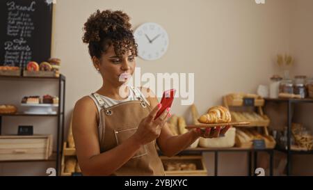 Una giovane donna in una panetteria che scatta una foto di un croissant con il suo cellulare Foto Stock