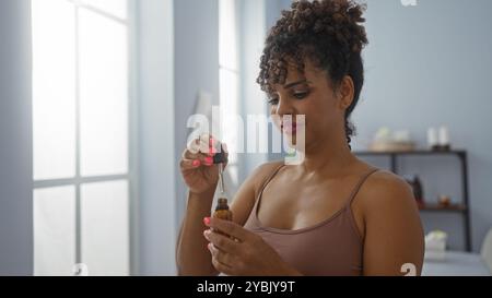 Bella donna con capelli bruna ricci in una stanza spa che applica con cura l'olio di una bottiglia contagocce, creando un'atmosfera di benessere serena all'interno Foto Stock