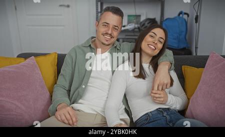 Una coppia sorridente siede a stretto contatto su un divano nel loro moderno soggiorno, ritraendo affetto e comfort. Foto Stock