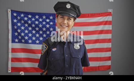 Poliziotta di mezza età sorridente che posa in uniforme di fronte a una bandiera americana al chiuso. Foto Stock