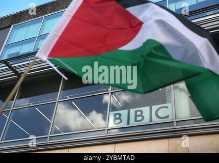 Birmingham, Inghilterra, Regno Unito. 19 ottobre 2024. Un manifestante inonda una bandiera palestinese di fronte agli uffici della BBC durante la manifestazione. I manifestanti si riuniscono per marciare contro la BBC e i media occidentali. I manifestanti sostengono che i media non sono stati nemmeno consegnati quando hanno riferito notizie dal Medio Oriente, distorcendo gli eventi a Gaza e in Libano a favore del regime israeliano. Credono che questo comportamento renda queste organizzazioni complici di quello che vedono come un genocidio del popolo palestinese. Foto Stock