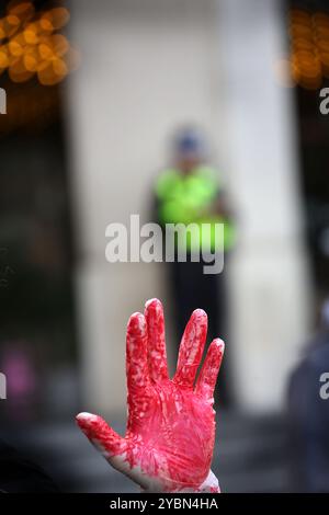 Birmingham, Inghilterra, Regno Unito. 19 ottobre 2024. Un manifestante tiene le mani rosse a significare il sangue sulle mani dei media, mentre un agente di polizia guarda da lontano durante la dimostrazione. I manifestanti si riuniscono per marciare contro la BBC e i media occidentali. I manifestanti sostengono che i media non sono stati nemmeno consegnati quando hanno riferito notizie dal Medio Oriente, distorcendo gli eventi a Gaza e in Libano a favore del regime israeliano. Credono che questo comportamento renda queste organizzazioni complici di quello che vedono come un genocidio del popolo palestinese. Foto Stock