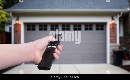 Mano che tiene in mano un telecomando, apre o chiude le porte del garage in un ambiente residenziale. Concetto di accesso automatico alla casa, comodità e tecnologia moderna Foto Stock