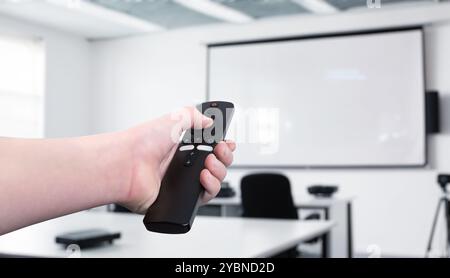 Mano con telecomando, proiettore in una sala conferenze o in una classe. Concetto di controllo della presentazione, riunione aziendale, istruzione, Foto Stock