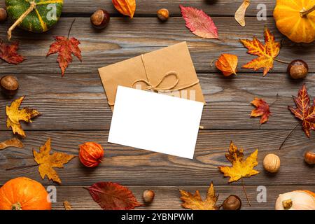 Biglietto d'auguri vuoto e busta nella cornice fatta di zucche, foglie essiccate, fiori, noci, castagne su fondo rustico in legno. Autunno e.. Foto Stock